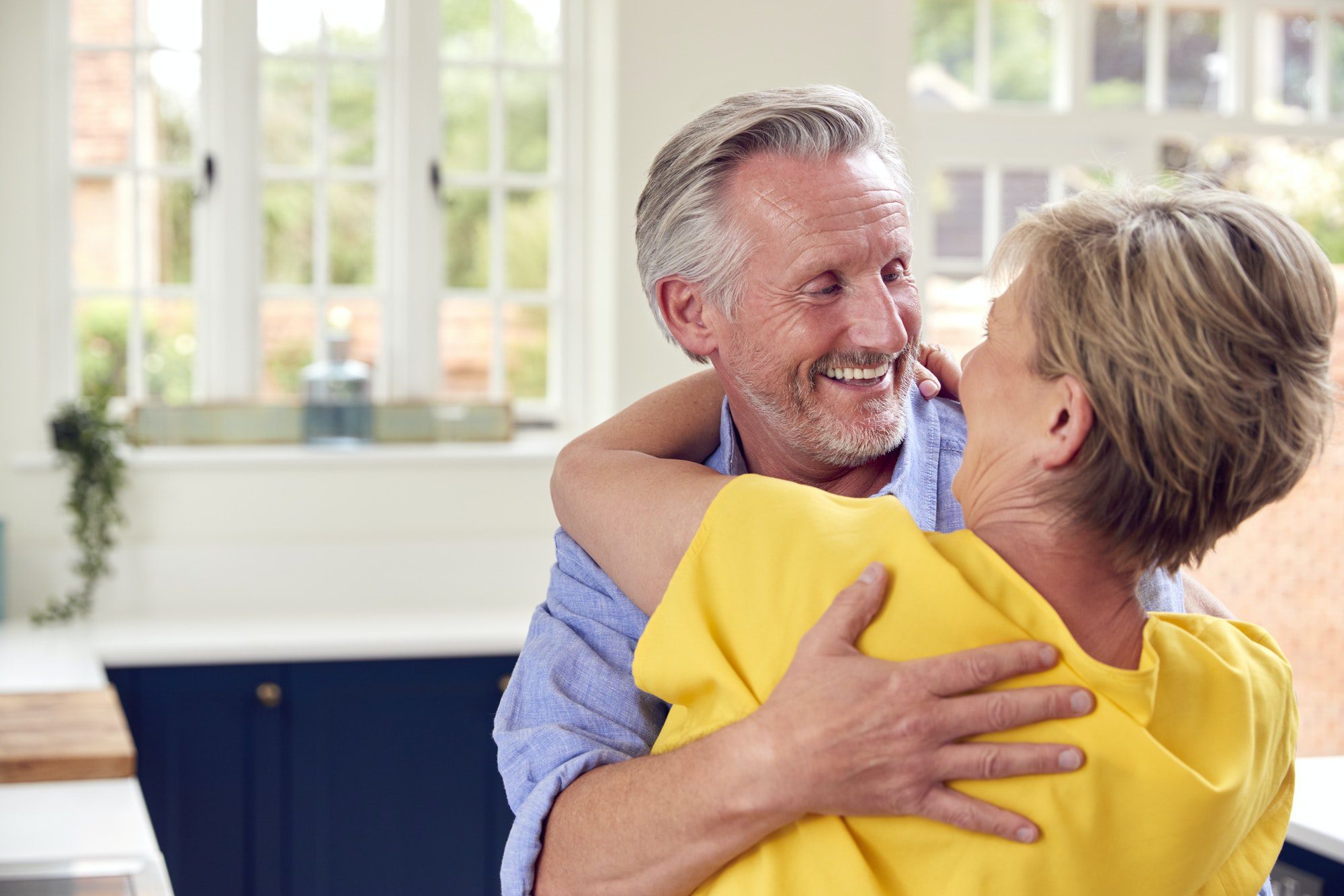 Loving Retired Couple Hugging In Kitchen At Home Together
