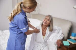 Krankenschwester, die einer älteren Frau bei einem Hausbesuch aus dem Bett hilft Perulatus